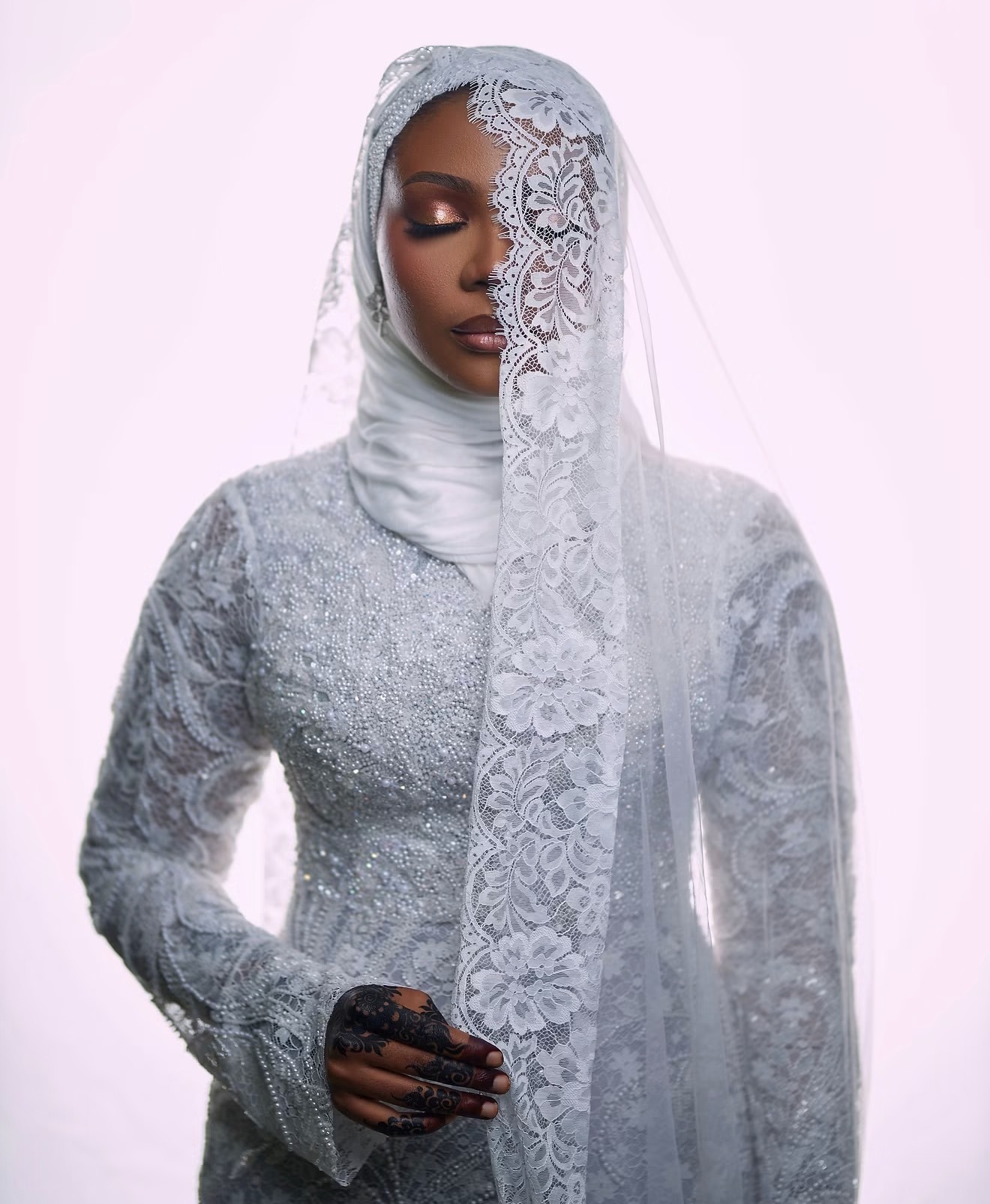 Bride in a beaded white gown and lace veil against a bright studio backdrop