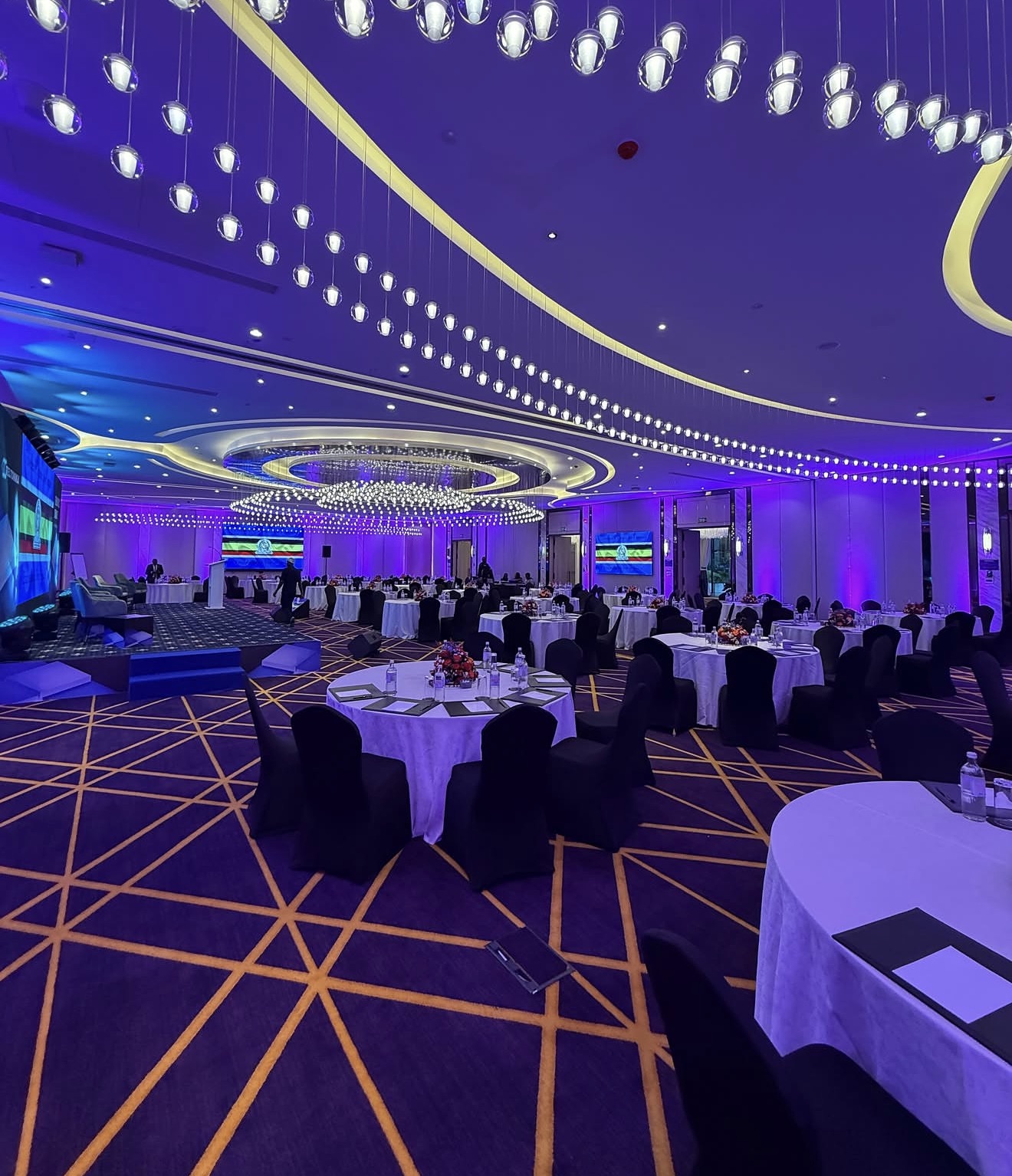 Conference venue with round tables, a stage, and suspended lighting