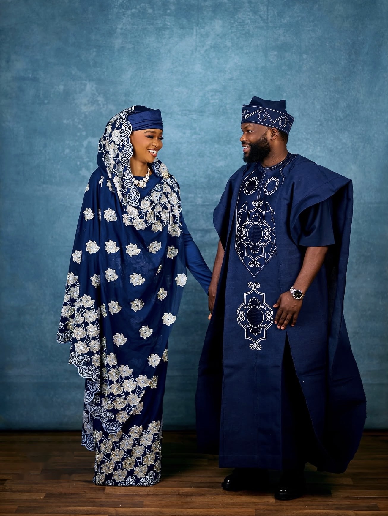 Couple in coordinated navy traditional attire with silver embroidery, holding hands